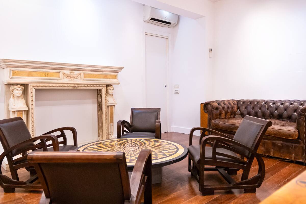 A room with a round table, four chairs, a fireplace, and a leather sofa.
