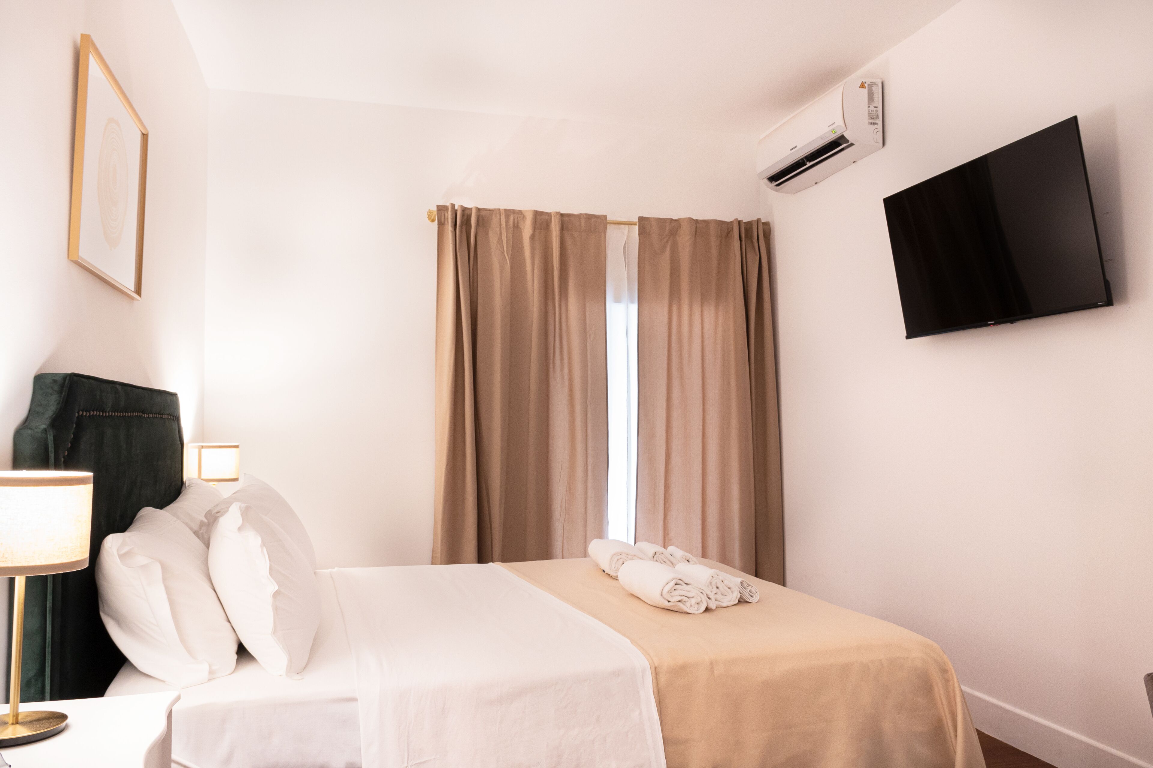 A hotel room with a bed, a TV, an air conditioner, and a window with curtains.