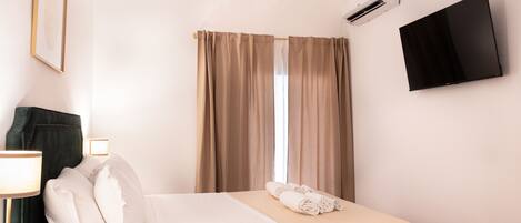 A hotel room with a bed, a TV, an air conditioner, and a window with curtains.