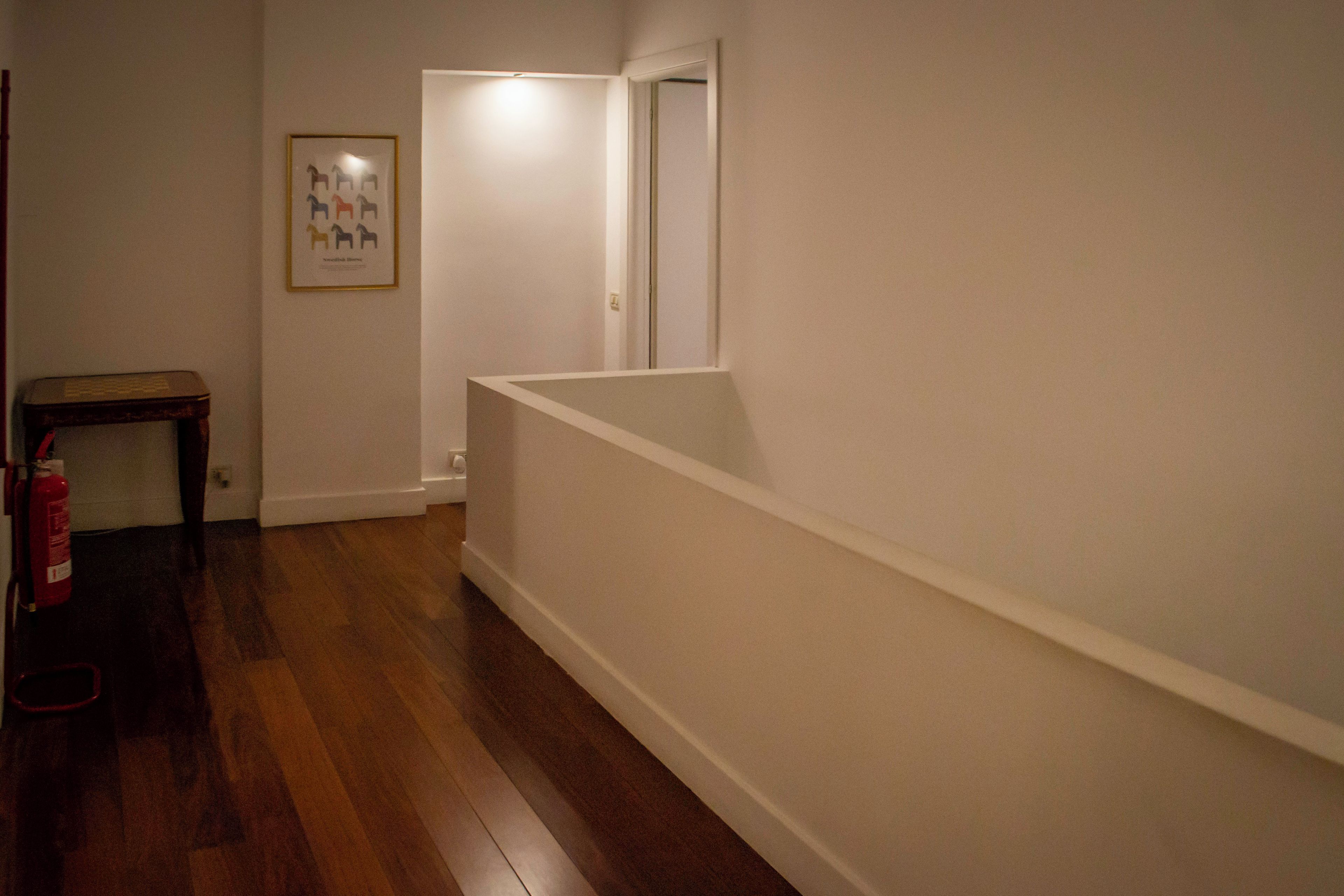 Un pasillo con piso de madera, un cuadro enmarcado en la pared y una puerta que da a otra habitación.