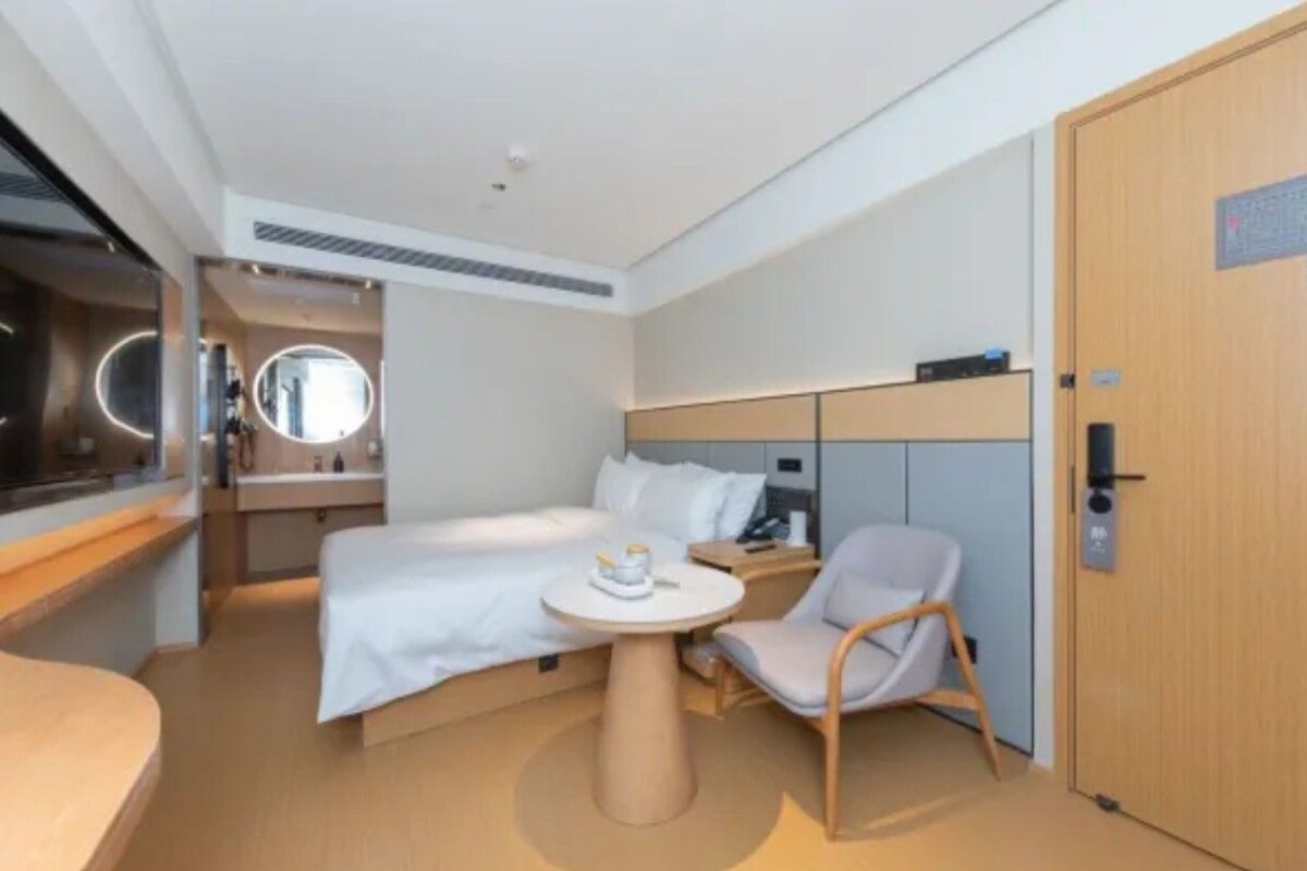 A modern hotel room with a bed, bedside table, chair, and a small round table.