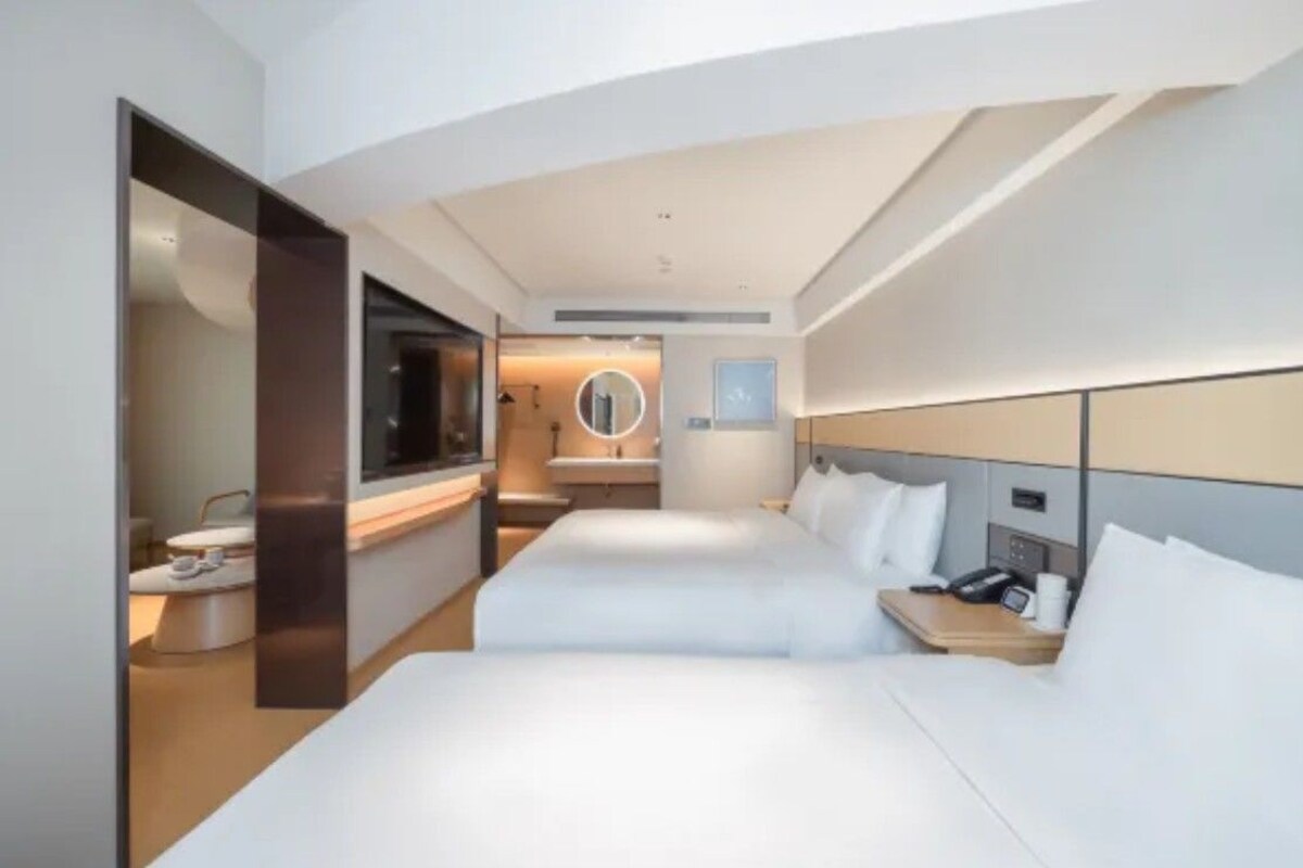 A hotel room with two beds, a bathroom, a TV, and a bedside table with a phone.