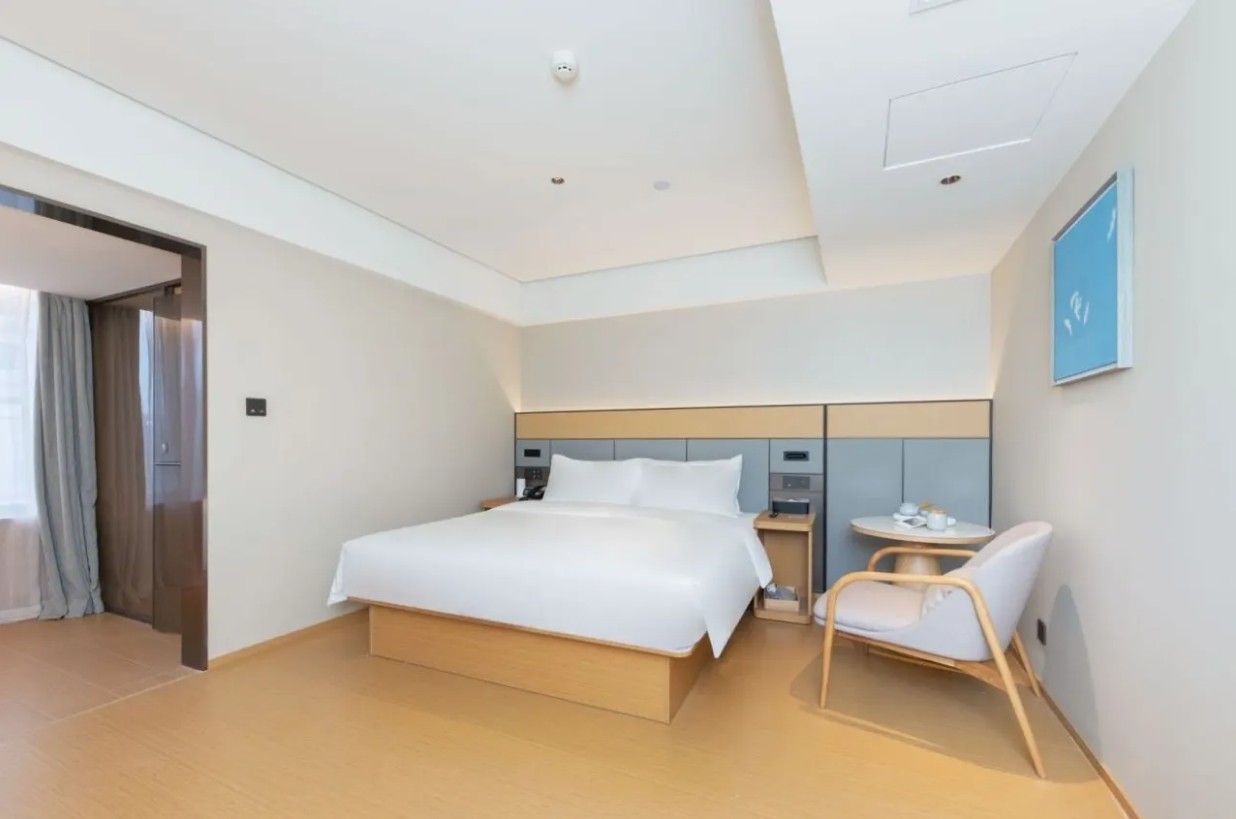 Una habitación de hotel moderna con una cama grande, mesitas de noche, una silla y una pequeña mesa con una taza y un plato.