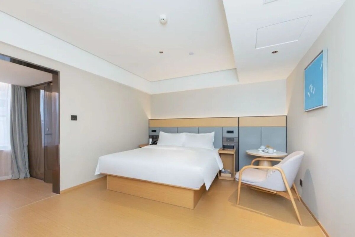 A modern hotel room with a large bed, bedside tables, a chair, and a small table with a cup and saucer.