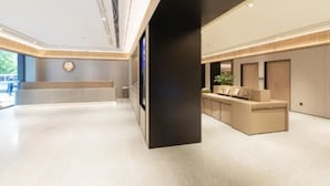 En modern hotellobby med en receptionsdisk, en stor svart pelare och en sittgrupp med utsikt över omgivningarna.