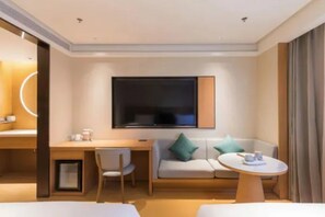 A modern hotel room with a flat-screen TV, a sofa, a desk, and a small round table. - Ji Hotel (Beijing)