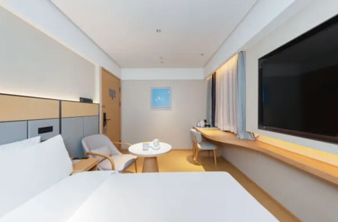 A hotel room with a bed, a desk, a chair, a small round table, and a large window.