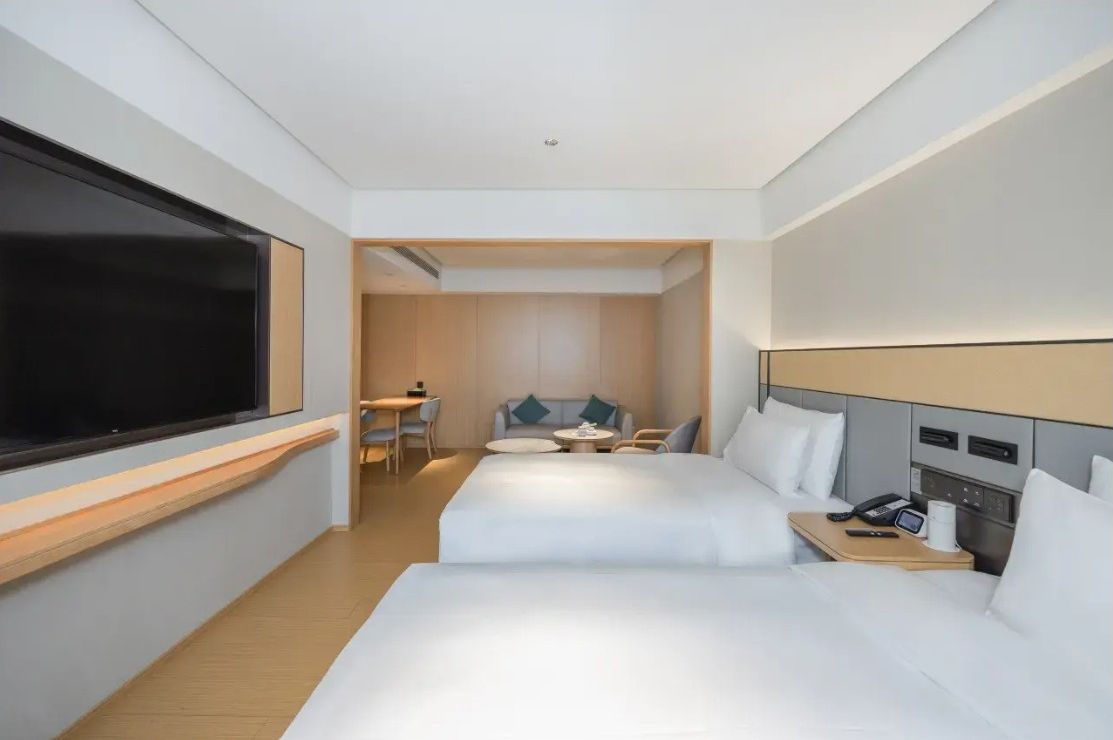 A hotel room with two beds, a desk, a chair, a small table, and a TV.