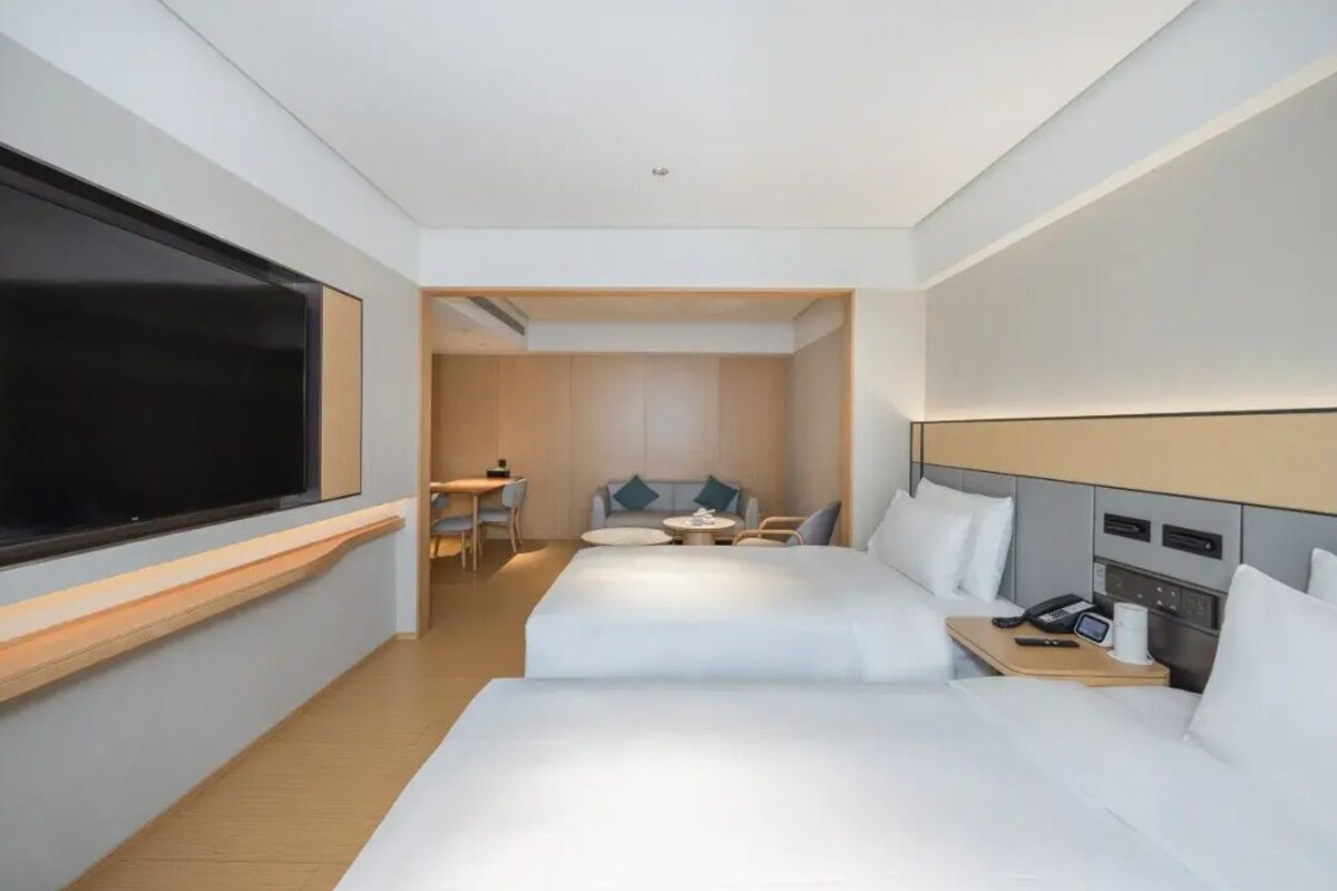 A hotel room with two beds, a desk, a chair, a small table, and a TV.