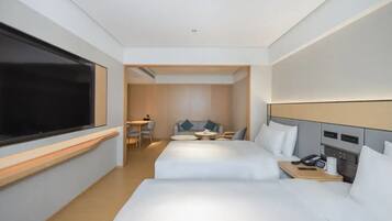 A hotel room with two beds, a desk, a chair, a small table, and a TV.