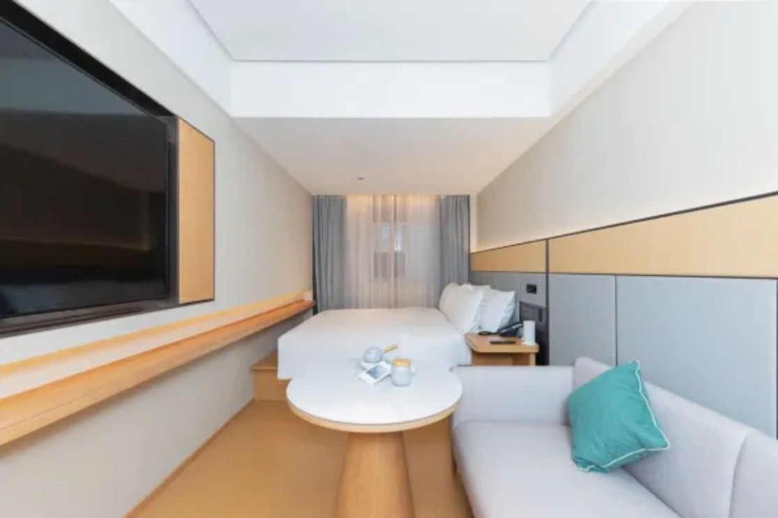 A modern hotel room with a bed, a small round table, a sofa, and a TV.