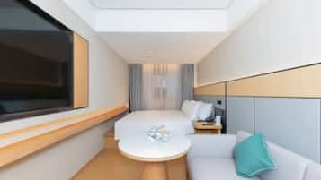 A modern hotel room with a bed, a small round table, a sofa, and a TV.