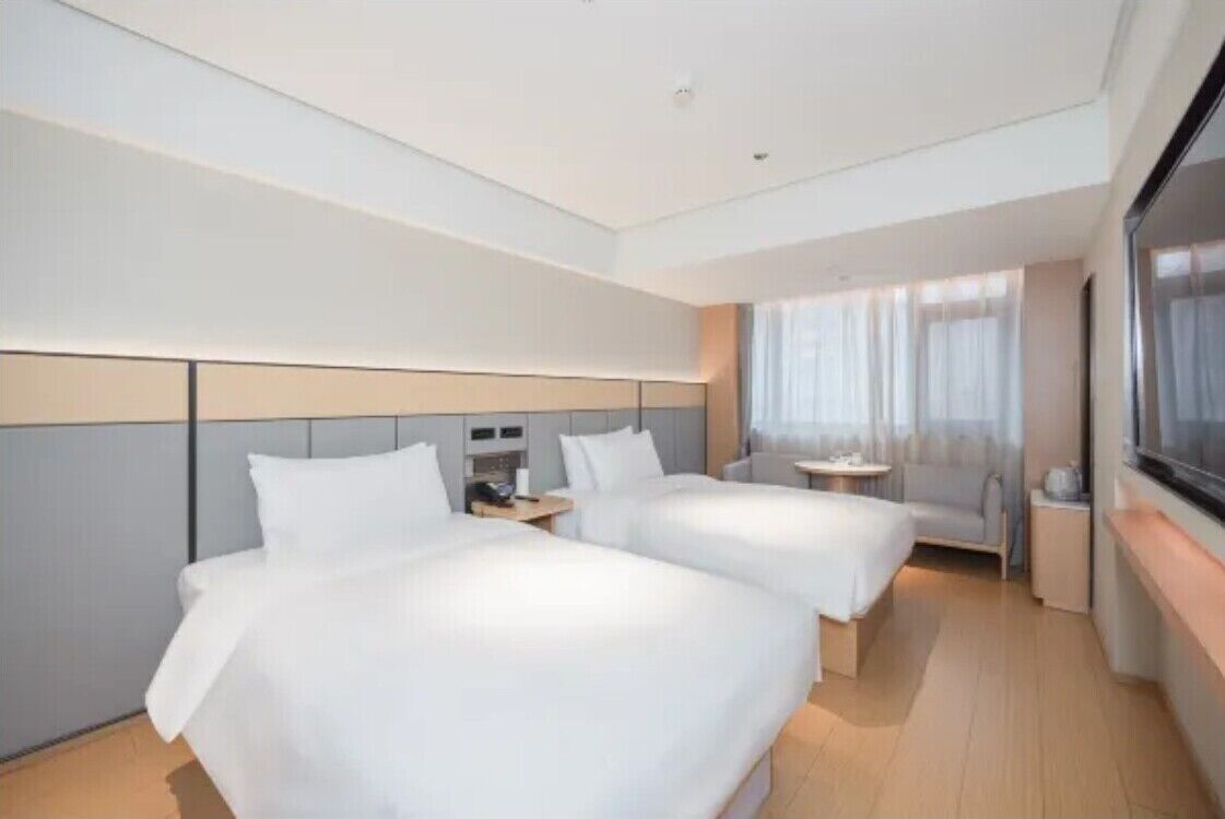 A hotel room with two beds, a sofa, a TV, and a window with curtains.