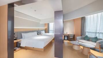 A modern hotel room with a large bed, a sofa, a coffee table, and a desk.