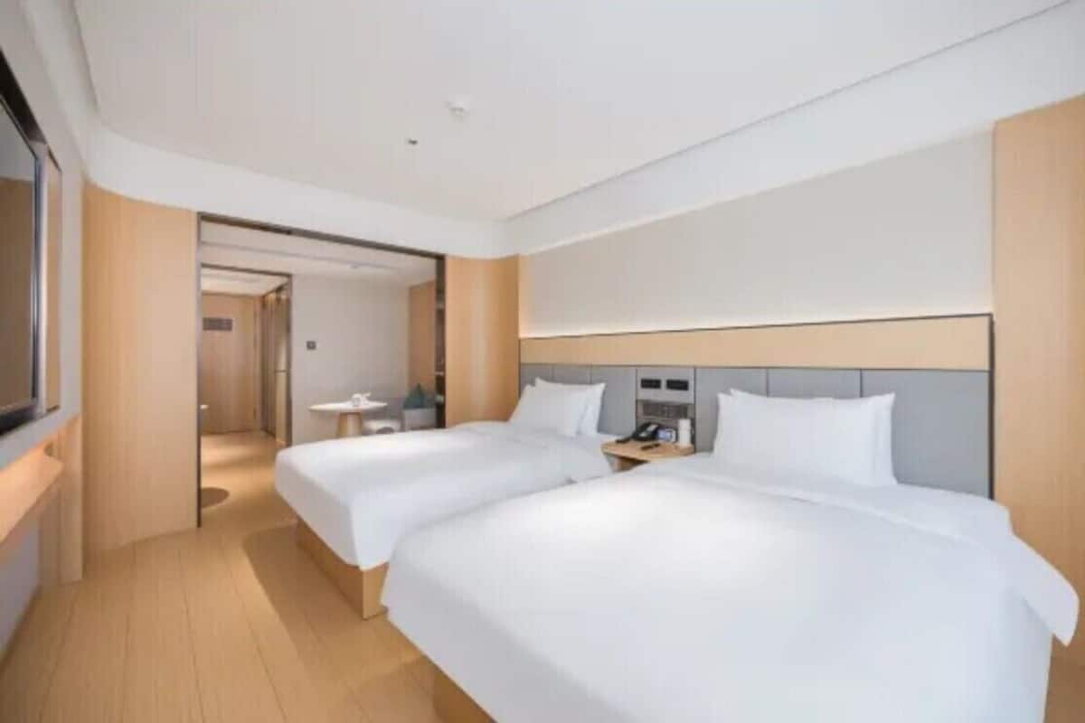 A hotel room with two beds, a bedside table with a phone, and a small table with a chair.