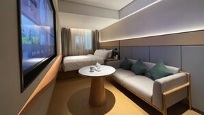 Ett modernt hotellrum med en säng, en soffa, ett soffbord och en stor TV-skärm.