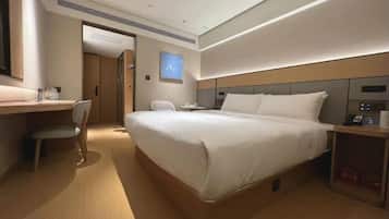 Een moderne hotelkamer met een groot bed, een bureau, een stoel en een bijzettafeltje met een telefoon en een lamp.