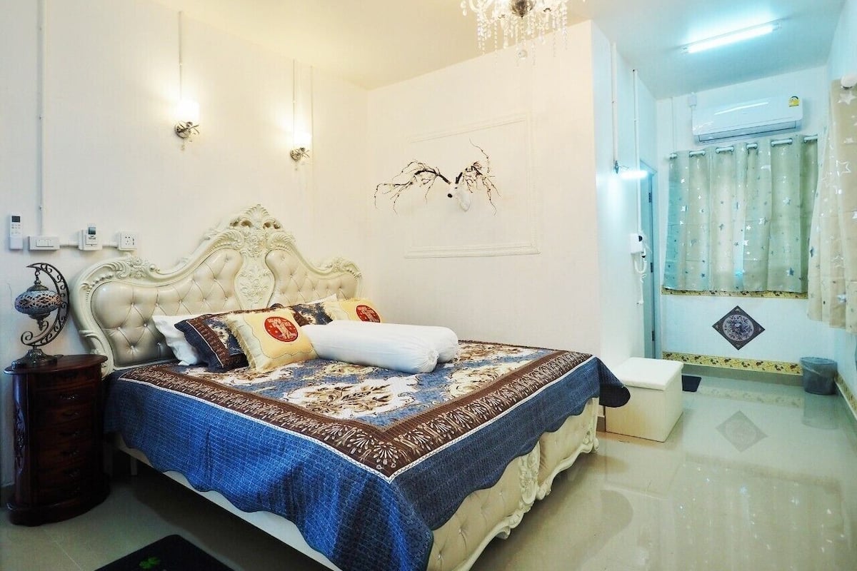 A bedroom with a large bed, a chandelier, a nightstand, and a wall-mounted light fixture.
