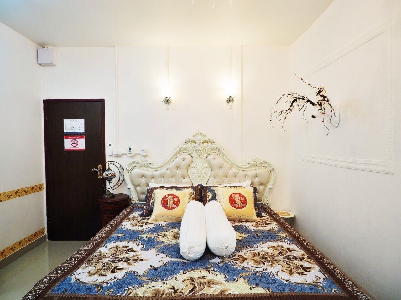 A bedroom with a large bed, a dark door, and a wall-mounted light fixture.