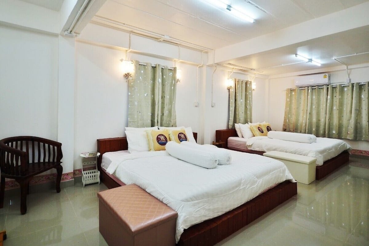 A hotel room with three beds, a wooden chair, a small table, and a bench.