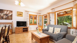 A living room with a sofa, TV, wooden coffee table, and a dining area with chairs and a table. - Margosa, Finca 5StarsHome Mallorca (Pollensa / Pollença)