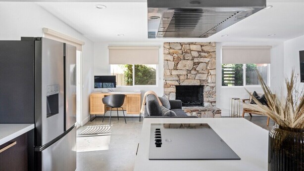 A modern kitchen with a built-in stove, a stone fireplace, and a dining area with a white table and chairs. - Kalima Sky - Golf Cart, Pool/Spa, Gym, Corner Lot (La Quinta)