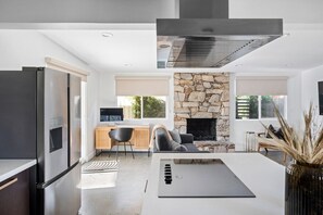 Uma cozinha moderna com fogão embutido, lareira de pedra e área de jantar com mesa e cadeiras brancas.