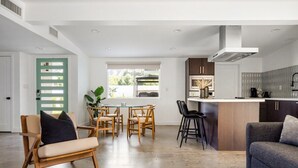 A modern kitchen with a central island, wooden dining chairs, and a grey sofa. - Kalima Sky - Golf Cart, Pool/Spa, Gym, Corner Lot (La Quinta)
