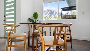 A dining area with a table and chairs, a potted plant, and a window with a mountain view. - Kalima Sky - Golf Cart, Pool/Spa, Gym, Corner Lot (La Quinta)