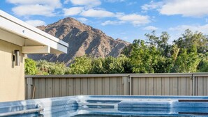 A swimming pool with a mountain backdrop, surrounded by a wooden fence and lush greenery. - Kalima Sky - Golf Cart, Pool/Spa, Gym, Corner Lot (La Quinta)