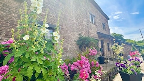 A rustic stone building with a brick facade, surrounded by vibrant flowering plants. - 16th Cent,6 bed house,15 People (Monmouthshire)