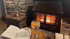 A cozy room with a stone wall, a fireplace, and a table with an open book and a glass of drink. - 16th Cent,6 bed house,15 People (Monmouthshire)