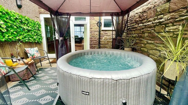 A hot tub in a covered outdoor area with wicker furniture and a stone wall.