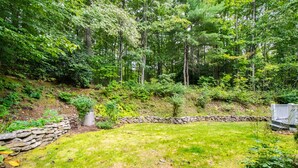 Ein Garten mit einer Steinsmauer, einem Rasen und verschiedenen Bäumen und Sträuchern.