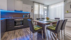 Una cucina moderna con forno integrato, microonde e una striscia luminosa blu a LED. C'è un tavolo da pranzo con sedie e una finestra con tende.