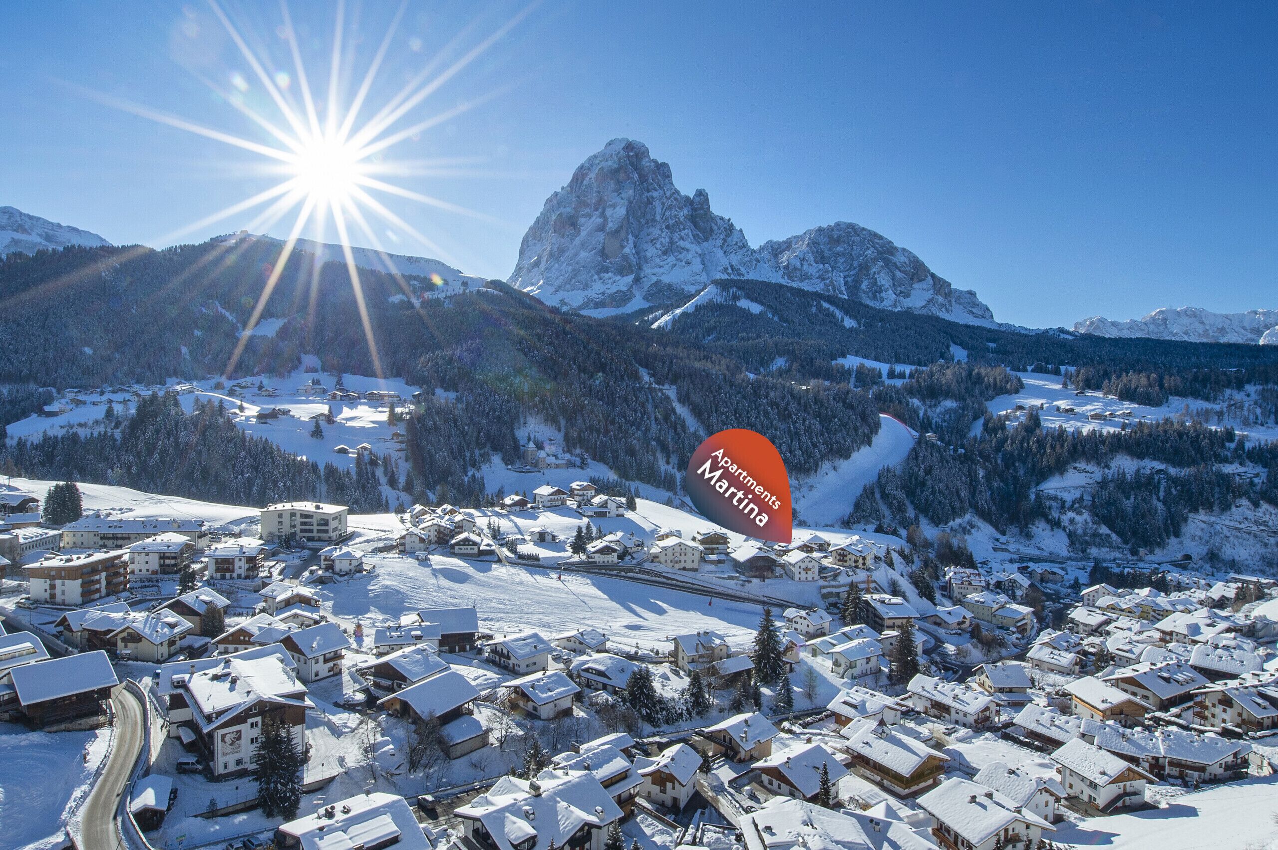 Un village enneigé, avec des bâtiments de style chalet traditionnel, un sommet montagneux imposant et un ciel bleu dégagé.
