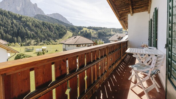 Een balkon met houten hekwerk met uitzicht op een bergachtig landschap.