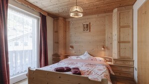 Een houten slaapkamer met een bed, een raam met gordijnen, een houten kledingkast en een hanglamp.