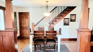 Un espace repas avec une table et des chaises en bois, un escalier et un lustre.