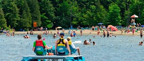 A lake with people on a blue raft and others swimming and sunbathing on the shore.