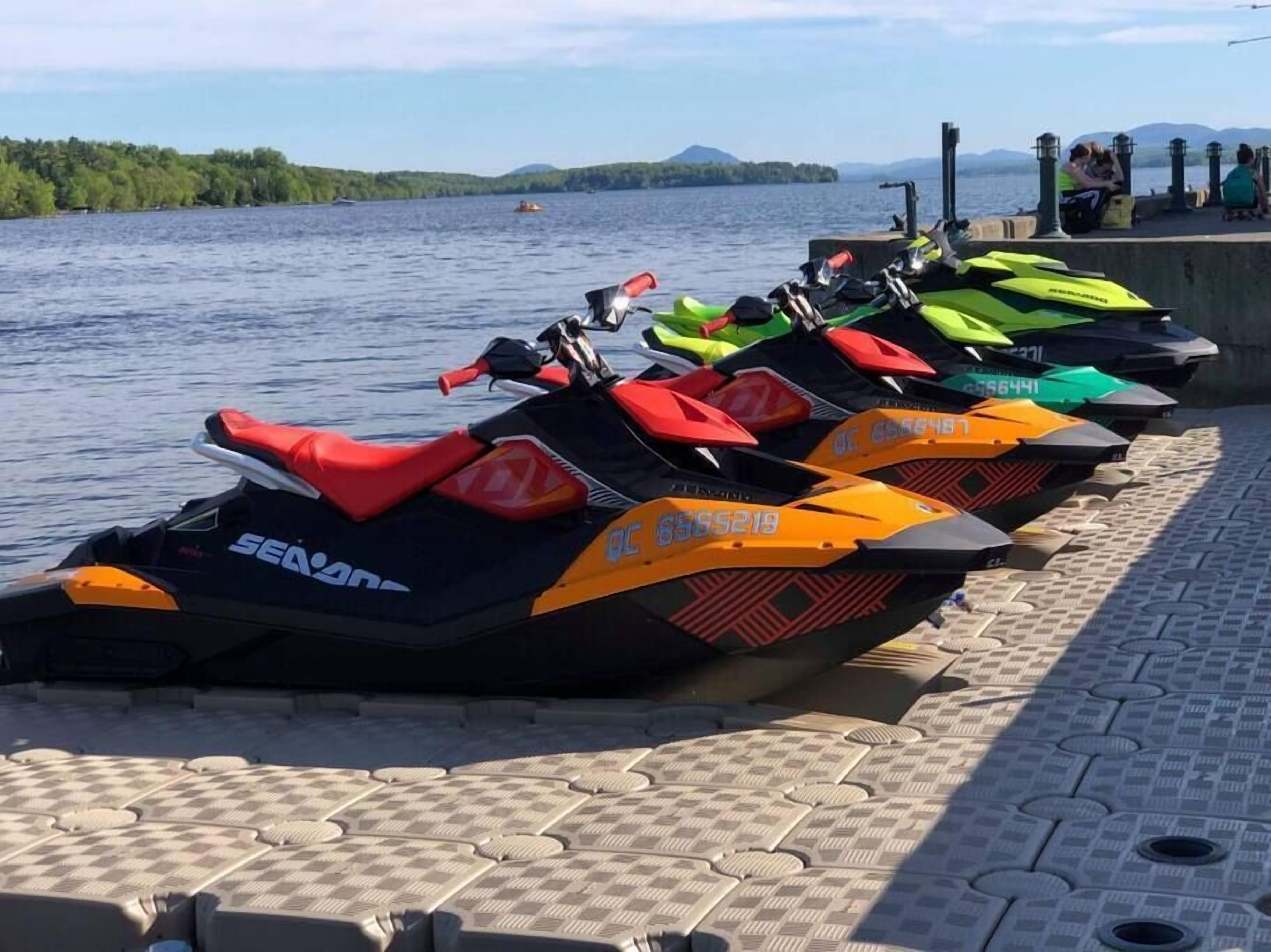 A row of jet skis lined up on a dock by a lake with a view of the water and distant mountains.