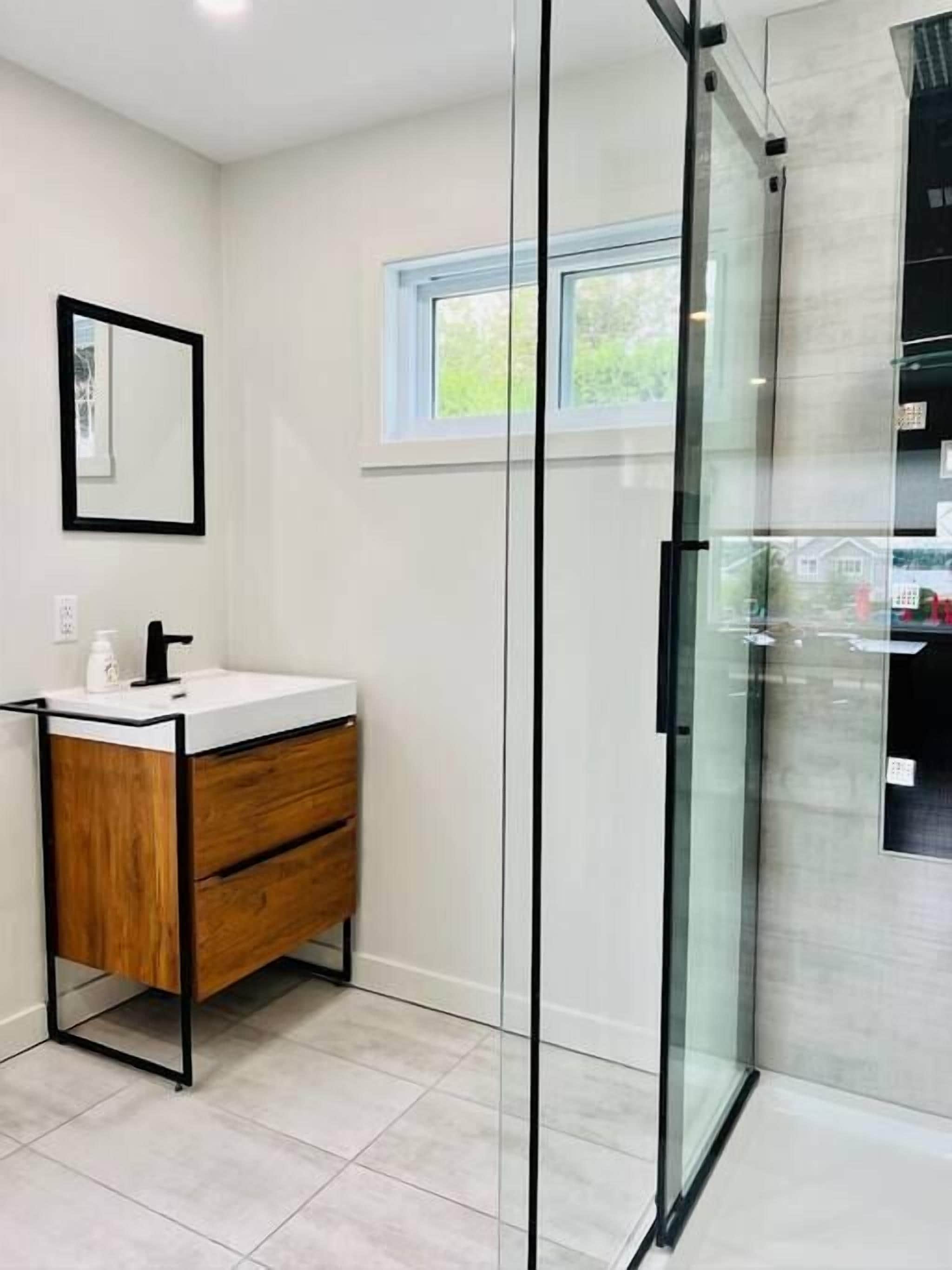 A modern bathroom with a glass shower enclosure, a wooden vanity, and a window providing natural light.