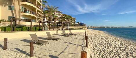 A beachfront hotel with multiple balconies, sun loungers, and a sandy beach.