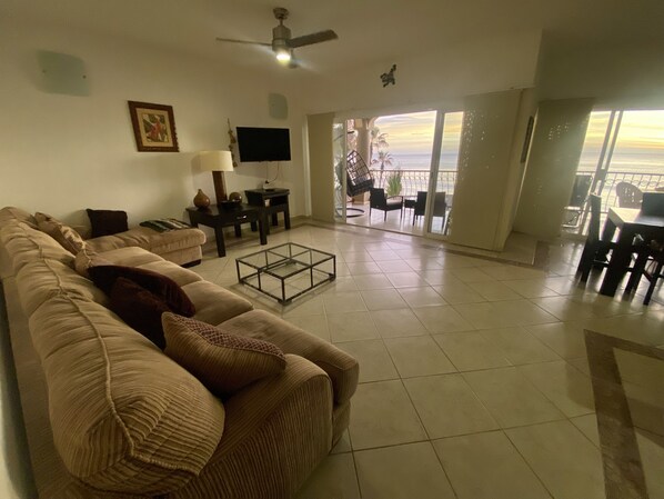 Un salon comprenant un canapé, une table basse, un téléviseur et un balcon aménagé avec du mobilier d’extérieur.