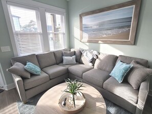 A living room with a sectional sofa, a coffee table with a plant, and a beach view painting.