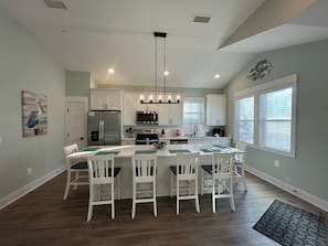 A modern kitchen with white cabinets, a central island with chairs, a stainless steel refrigerator, and a hanging light fixture.