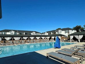 Une piscine entourée de chaises longues et de parasols, elle-même bordée d’immeubles présentant un style architectural uniforme.