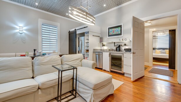 A modern living room with a sofa, a glass coffee table, a kitchen area with appliances, and a dining area with a bench. - Cozy + Modern Norcross Hideaway w/ Covered Porches (Norcross)