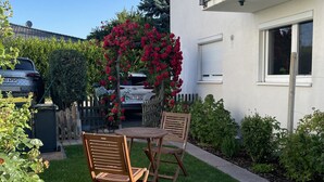 Une propriété résidentielle dotée d’une pelouse bien entretenue, d’une table et de chaises en bois, d’une arche fleurie et d’un balcon avec une balustrade.