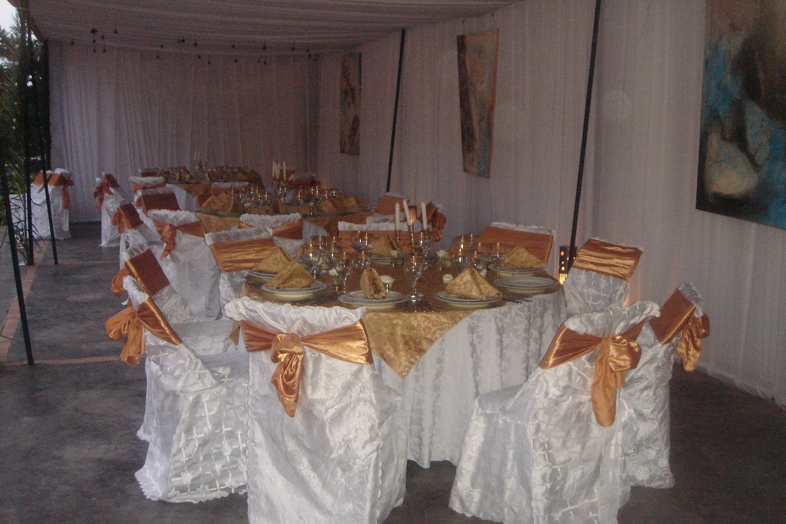 Un salón de banquetes con mesas dispuestas para un evento formal, con manteles blancos y fajas doradas.